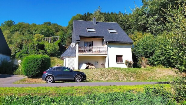 A two-story house with a balcony, a car parked in front, and lush greenery surrounding the property. - Maison 7 Personnes - Quartier Calme - Belle vue sur Charlannes (Murat-le-Quaire)