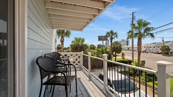 A wooden porch with two black wicker chairs and a small table, overlooking a street with palm trees and a sign for a local business. - Ocean view, great location, near Pier Park (Panama City Beach)