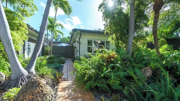 A tropical garden with a pathway leading to a house. - Charming Studio Prime Location Steps from Beach (Fort Lauderdale)