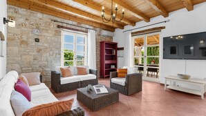 A spacious living area with a stone wall, wooden ceiling, and large windows offering a view of greenery. - Beautiful Villa Habibi with pool (Sovinjak)
