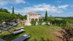 A stone villa with a swimming pool, surrounded by lush greenery and a clear sky.