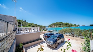 A coastal property with a paved driveway, two parked cars, and a view of the sea and a hilly landscape. - Holiday House with Sea View (Vela Luka)