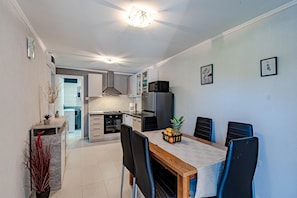 A modern kitchen with a dining area, featuring a wooden table, black chairs, and a refrigerator.