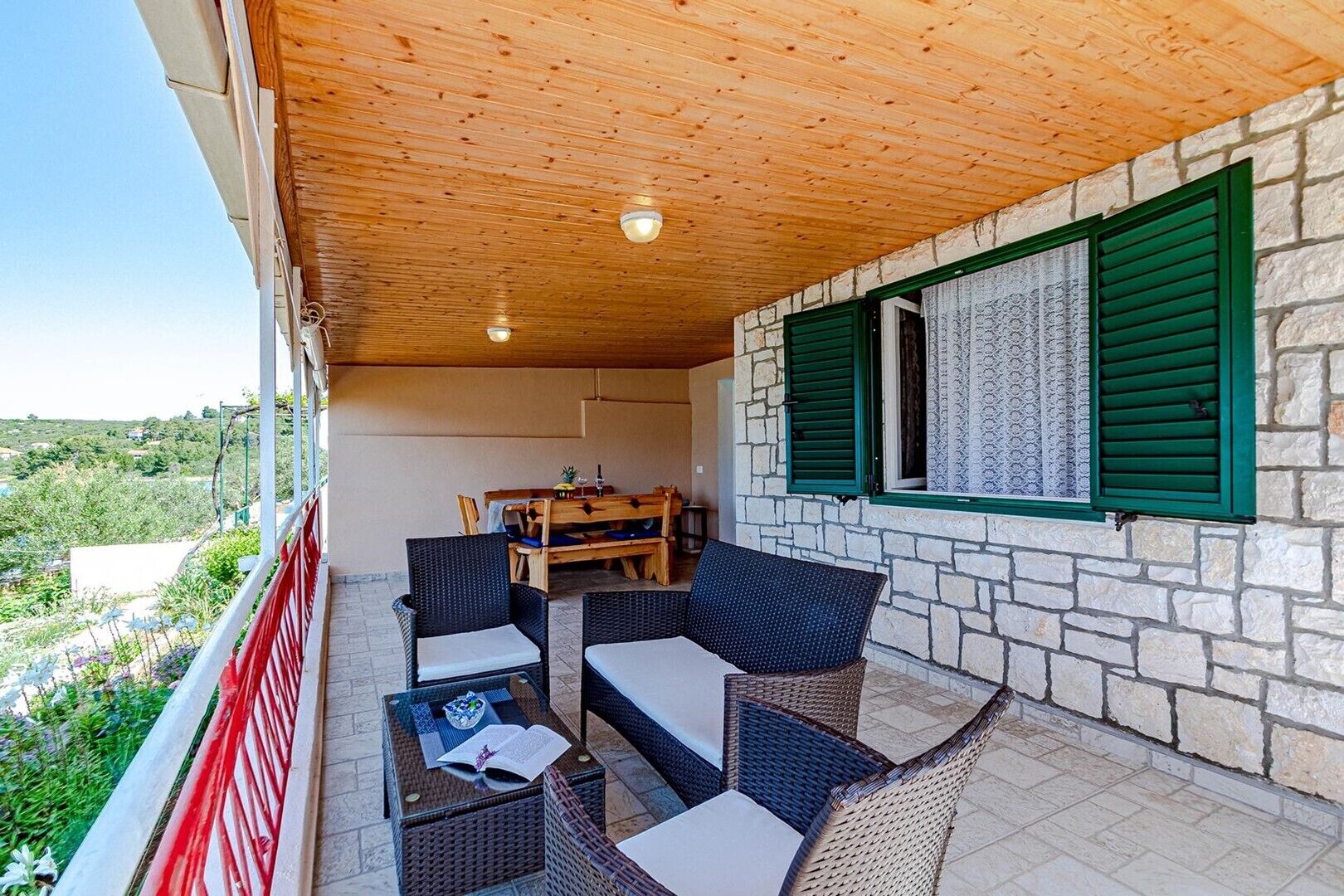 A covered outdoor seating area with wicker furniture, a table, and a view of the landscape.