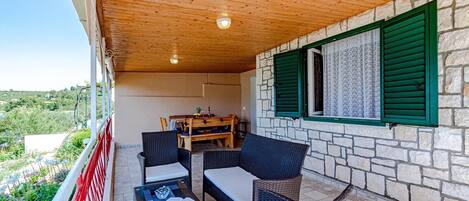 A covered outdoor seating area with wicker furniture, a table, and a view of the landscape.