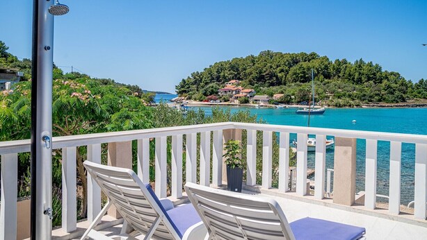 A balcony with white railings, two lounge chairs, and a water feature. - Holiday House with Sea View (Vela Luka)