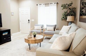 A living room with a beige sofa, two armchairs, a coffee table, a TV stand, and a door. - Stylish 3BR Disney Retreat with Resort Pool (Four Corners)