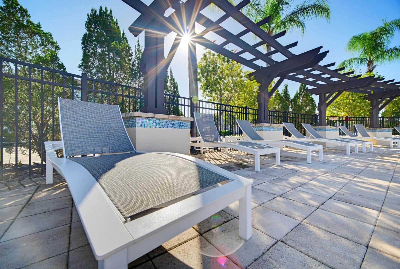 A sunlit outdoor lounge area with white lounge chairs and a pergola structure.