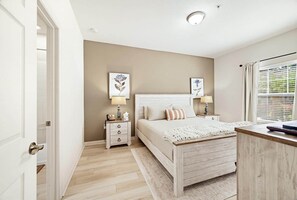 A bedroom with a bed, bedside tables, a nightstand, a window with blinds, and a door.