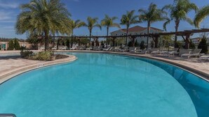 A clear blue swimming pool with lounge chairs and palm trees.