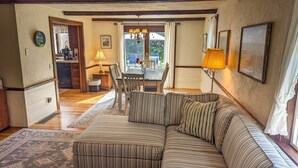 A cozy living room with a striped sofa, a dining table with chairs, a kitchen area, and a view through a glass door.