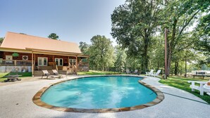 Ein Swimmingpool mit Holzterrasse und Liegestühlen, umgeben von einem Haus mit rotem Dach und einem eingezäunten Garten.