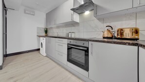 A modern kitchen with white cabinets, a built-in oven, a coffee maker, and a toaster. - Lovely 1-bed Studio in Feltham (Feltham)