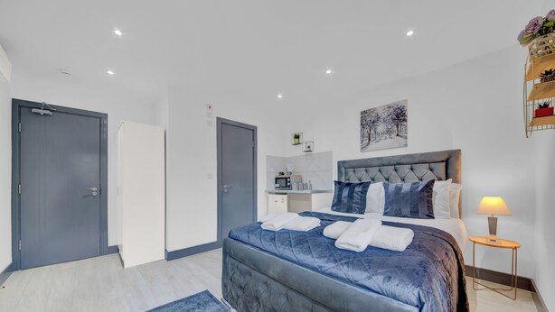 A modern bedroom with a large bed, a bedside table, and a small desk area. - Lovely 1-bed Studio in Feltham (Feltham)