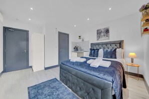 A modern bedroom with a large bed, a bedside table, and a small desk area. - Lovely 1-bed Studio in Feltham (Feltham)