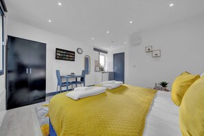 A modern hotel room with a large bed, a desk with a chair, a wardrobe, and a small kitchenette. - Inviting 1-bed House in Feltham (Feltham)