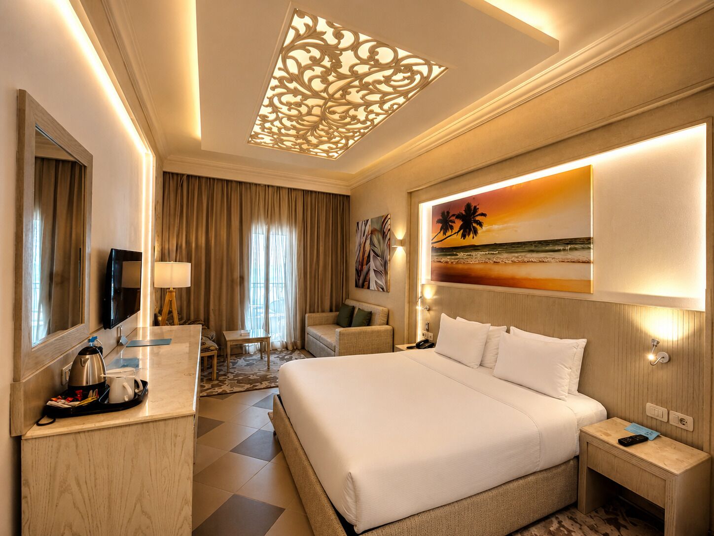 A hotel room with a large bed, a desk with a coffee maker, a TV, and a painting of a beach scene.