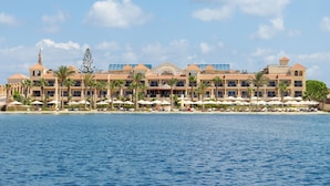 Ett stort hotellkomplex med flera balkonger, ett poolområde med parasoller och utsikt över havet.