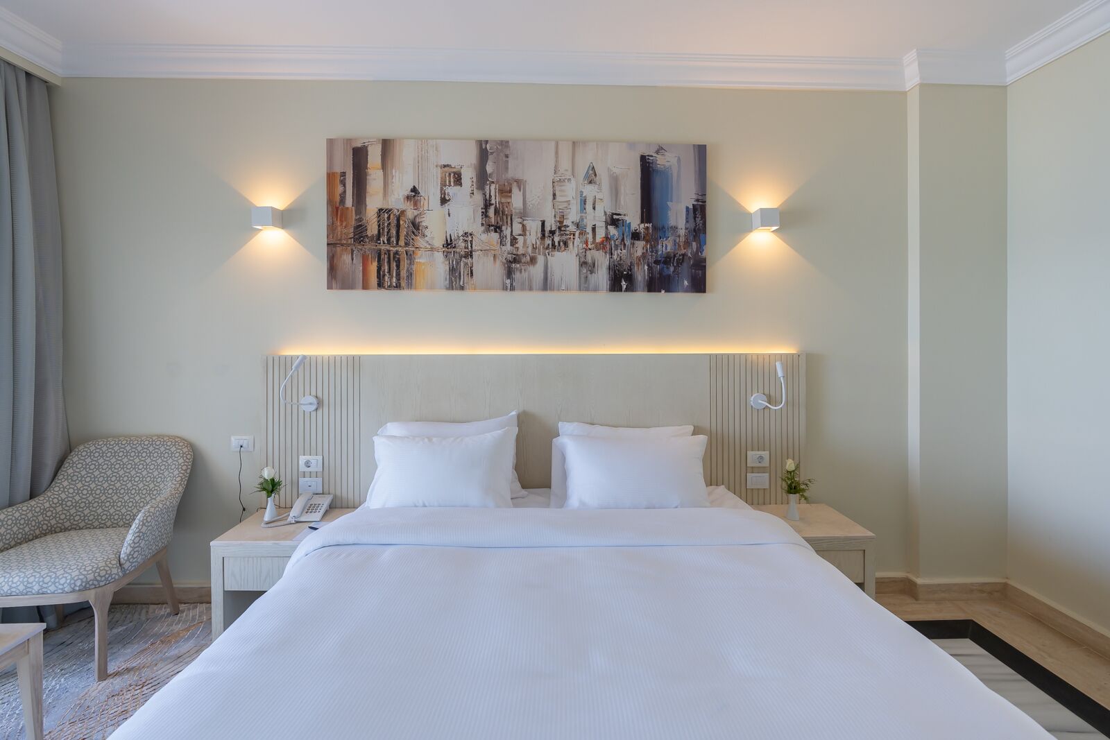 A hotel room with a large bed, two bedside tables, a chair, and a painting on the wall.