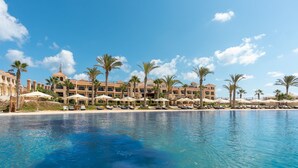 Ett semesterhotell med pool, palmer och en byggnad med flera balkonger.