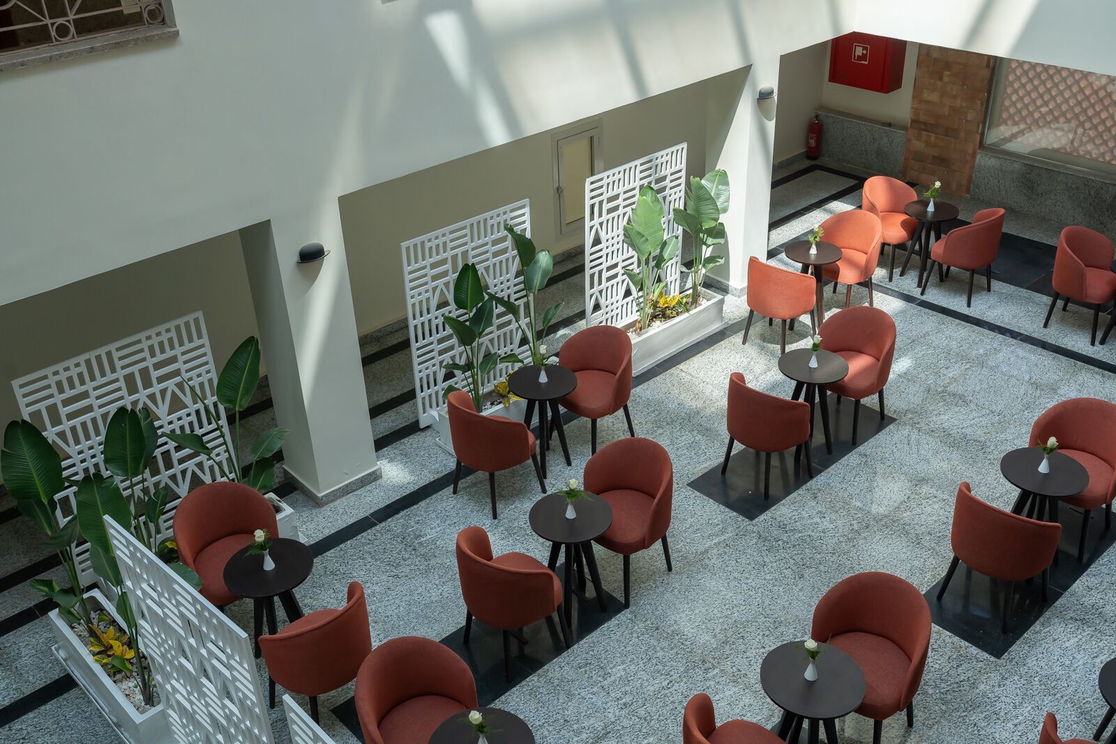 A spacious indoor area with multiple tables and chairs, white decorative partitions, and potted plants.