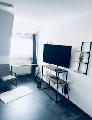 A modern living room with a flat-screen TV, a sofa, a coffee table, and a potted plant.