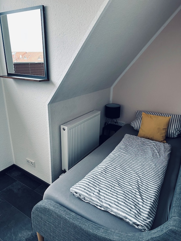 A bedroom with a bed, a radiator, a lamp, and a window.