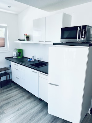 A modern kitchen with white cabinetry, a black countertop, a coffee maker, and a microwave.