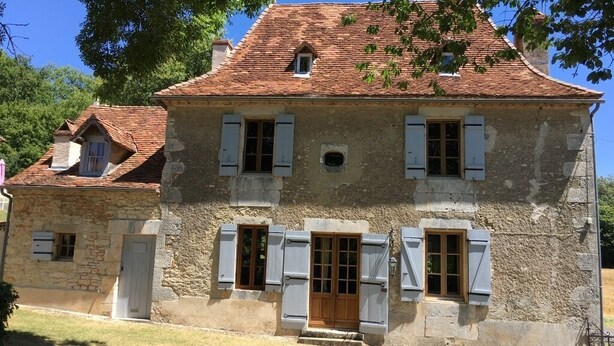 A stone building with a tiled roof, multiple windows with shutters, and a central wooden door. - Maison Périgourdine en Pierre Nature Avec Piscine (Saint-Jory-las-Bloux)