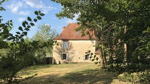 A rustic house with a tiled roof, surrounded by trees and a grassy yard. - Maison Périgourdine en Pierre Nature Avec Piscine (Saint-Jory-las-Bloux)