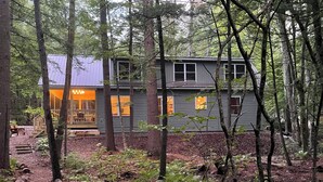 A cabin with a deck and a covered outdoor seating area, surrounded by a forest.