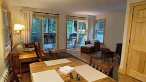 A cozy dining area with a wooden table, chairs, and a bench. There are two lamps on the wall, and a door leading to an outdoor patio.