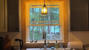 A kitchen with a large window, a sink, and a hanging light fixture.