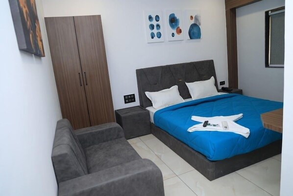 Un dormitorio con cama, sofá gris, armario y una obra de arte en la pared.
