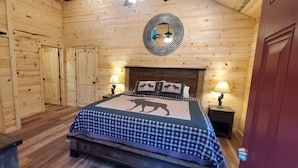 Een houten kamer met een bed, twee nachtkastjes, een spiegel en een deur.