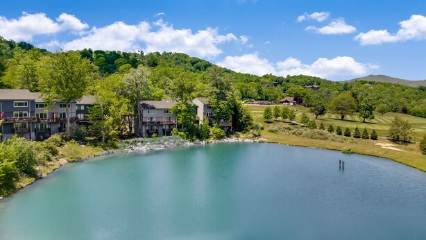 A lakeside property with modern buildings, a golf course, and a forested hill. - Cozy Sugar Ski - 4 Ensuites, Extremely close to Slopes, Tubing, and Ice Skating! (Sugar Mountain)