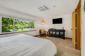 Une chambre à coucher avec un grand lit, une commode, une chaise, un téléviseur et une fenêtre donnant sur un paysage verdoyant.