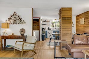 Un salon moderne avec un plancher en bois, un canapé, un fauteuil, une table basse et un élément décoratif mural.