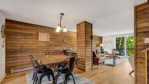 A modern interior with a wooden wall, a dining area with a table and chairs, a sofa, and a window with a view of greenery. - Cozy Sugar Ski - 4 Ensuites, Extremely close to Slopes, Tubing, and Ice Skating! (Sugar Mountain)