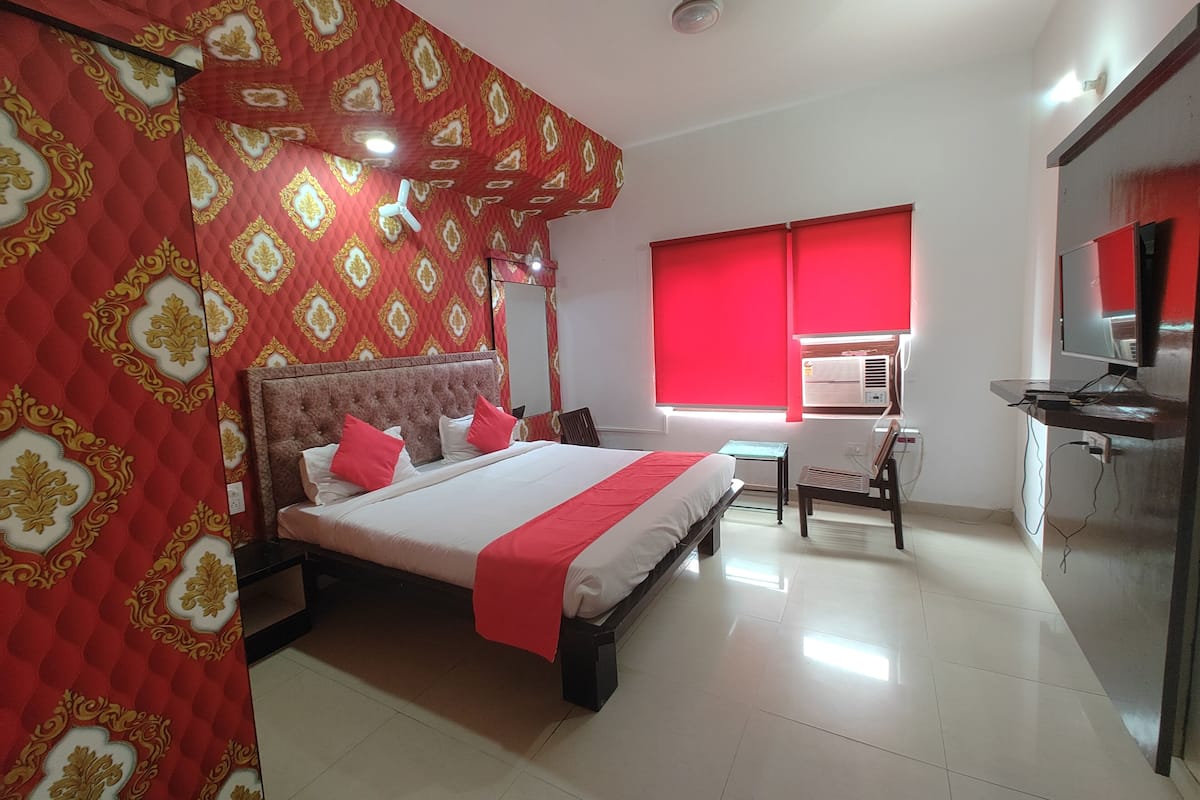 Habitación de hotel con una cama grande, un escritorio con silla, un televisor y una ventana con persianas rojas.
