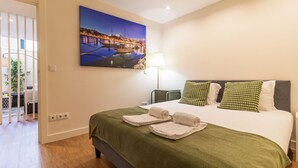 A hotel room with a bed, green bedding, a painting of a cityscape, and a lamp. - Delightful Duplex by LovelyStay (Vila Nova de Gaia)