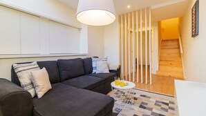 A modern living room with a dark grey sofa, a white coffee table with drinks, and a patterned rug. - Delightful Duplex by LovelyStay (Vila Nova de Gaia)