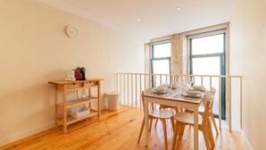 A dining area with a wooden table set for four, a small shelf with kitchen items, and a window with a view. - Delightful Duplex by LovelyStay (Vila Nova de Gaia)