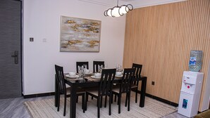 Un coin repas avec une table dressée pour six personnes, des chaises, un distributeur d’eau et un tableau accroché au mur.