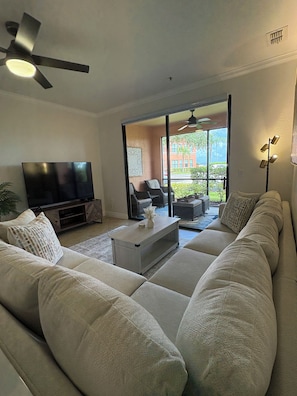 A living room with a large sectional sofa, a flat-screen TV, a ceiling fan, and a sliding glass door leading to an outdoor area.