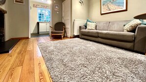 A living room with a grey sofa, a wooden floor, a grey carpet, a wooden chair, and a painting on the wall. - 1 Dolphin Cottages (Lyme Regis)