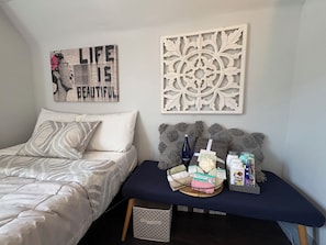 A bedroom with a bed, pillows, a bedside table with toiletries, and decorative wall art.