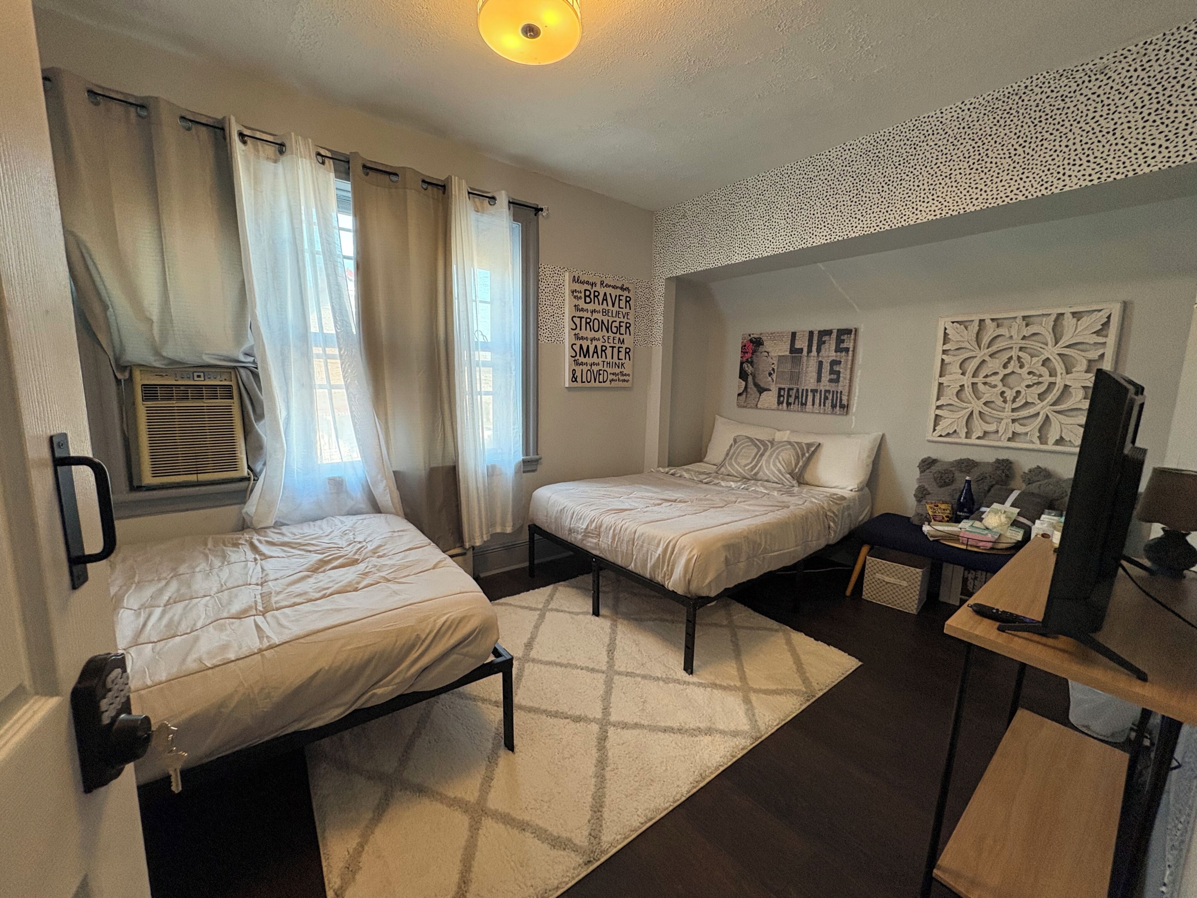 A bedroom with two beds, a desk, a television, and decorative wall art.