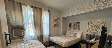 A bedroom with two beds, a desk, a television, and decorative wall art.