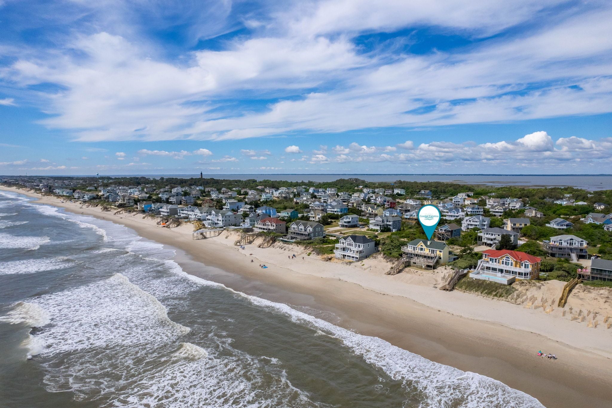 A coastal residential area with beachfront properties, a lighthouse, and a clear sky.
